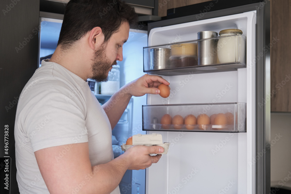 Young latin man placing eggs in the fridge door shelf. Young latin man placing eggs in the fridge door shelf.