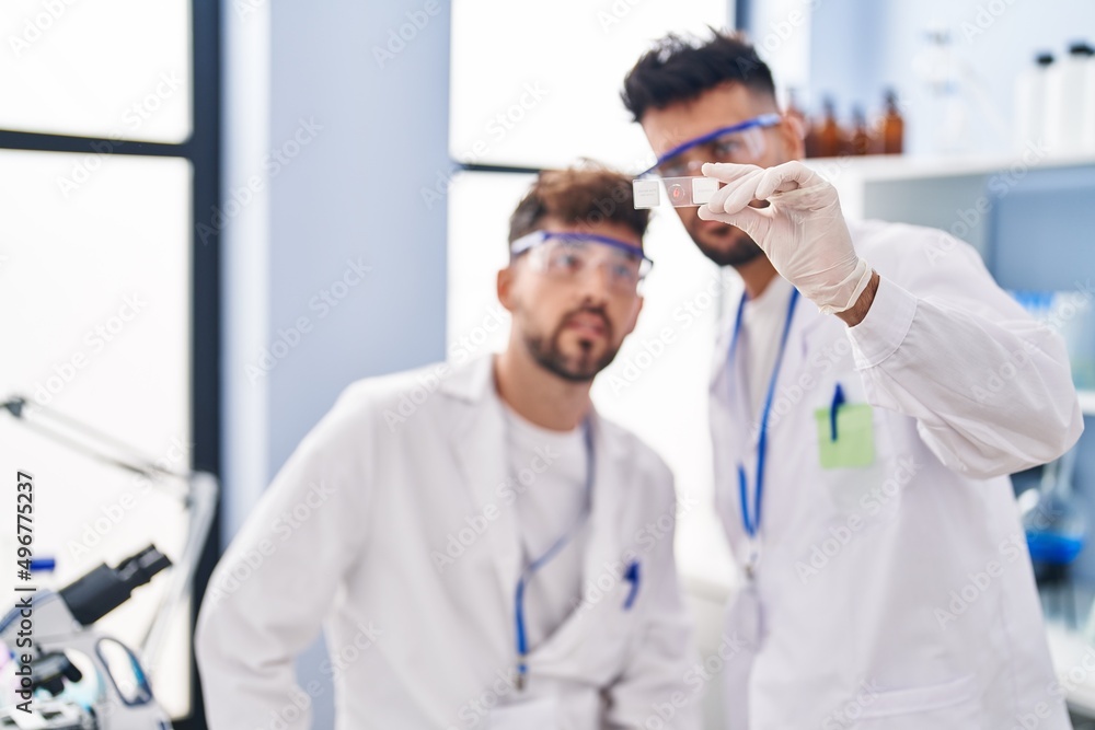 Young couple wearing scientist uniform holding sample at laboratory Young couple wearing scientist uniform holding sample at laboratory
