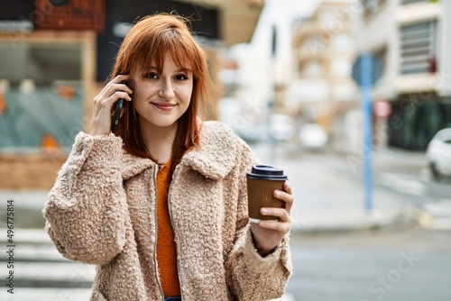 Young redhead girl talking on the smartphone drinking coffee at the city.