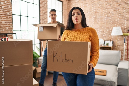 Young couple moving to a new home with cardboard boxes making fish face with mouth and squinting eyes, crazy and comical. © Krakenimages.com