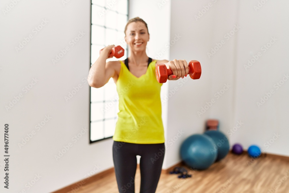 Young blonde girl smiling happy training using dumbbells at sport center. Young blonde girl smiling happy training using dumbbells at sport center.