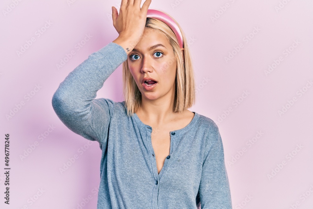 Beautiful blonde woman standing over pink background surprised with hand on head for mistake, remember error. forgot, bad memory concept. Beautiful blonde woman standing over pink background surprised with hand on head for mistake, remember error. forgot, bad memory concept.