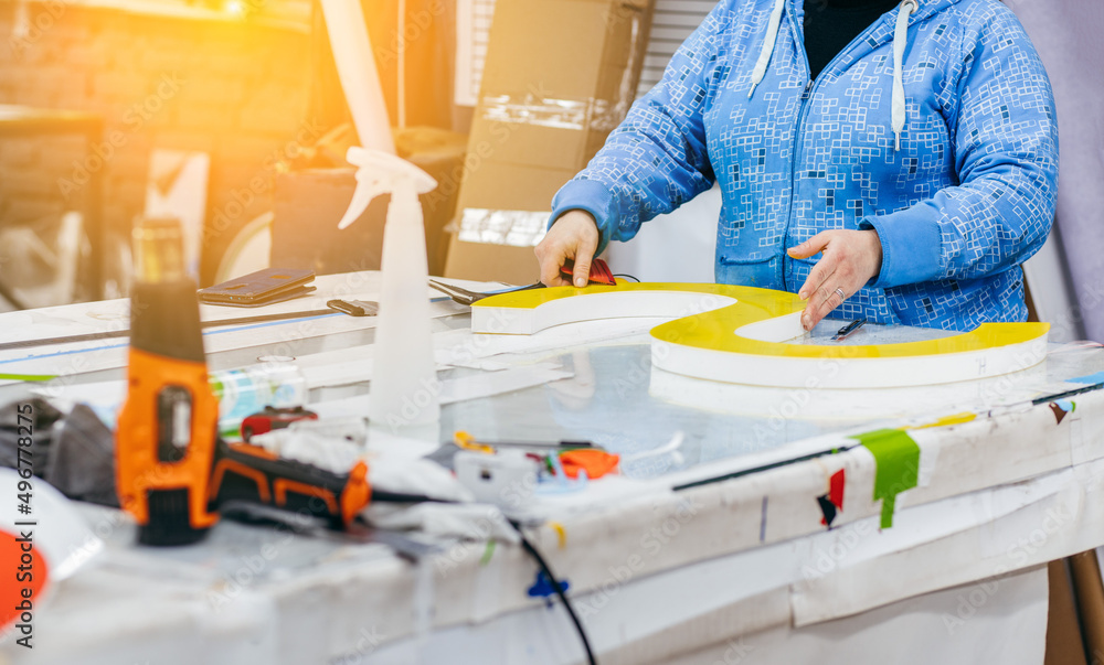 Applying colored yellow membrane to a surface of plastic 3d letter of signboard. worker's hands close up Applying colored yellow membrane to a surface of plastic 3d letter of signboard. worker's hands close up