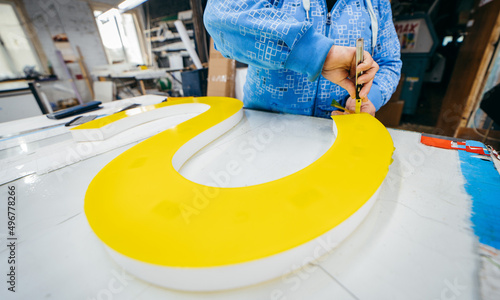 Applying colored yellow membrane to a surface of plastic 3d letter of signboard. worker's hands close up photo