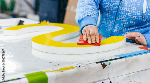 Applying colored yellow membrane to a surface of plastic 3d letter of signboard. worker's hands close up photo