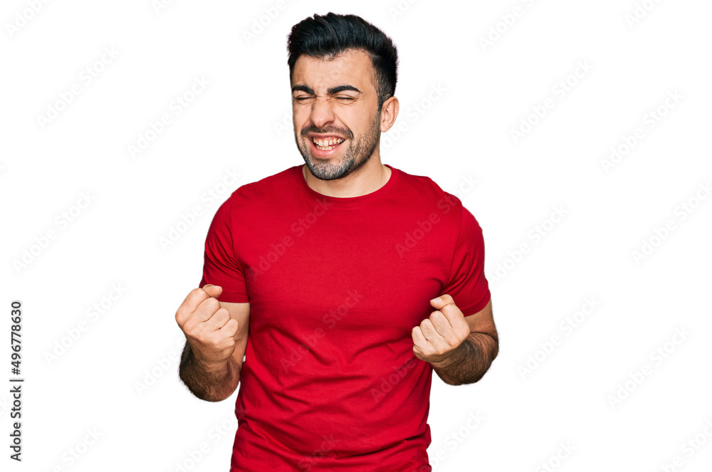 Hispanic man with beard wearing casual red t shirt excited for success with arms raised and eyes closed celebrating victory smiling. winner concept. Hispanic man with beard wearing casual red t shirt excited for success with arms raised and eyes closed celebrating victory smiling. winner concept.