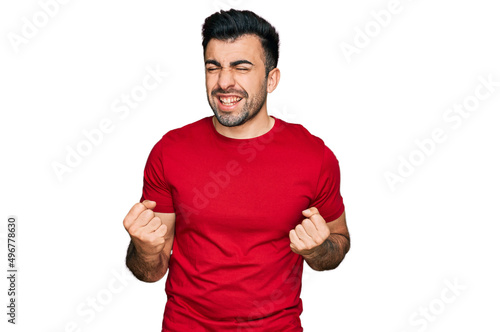 Hispanic man with beard wearing casual red t shirt excited for success with arms raised and eyes closed celebrating victory smiling. winner concept.