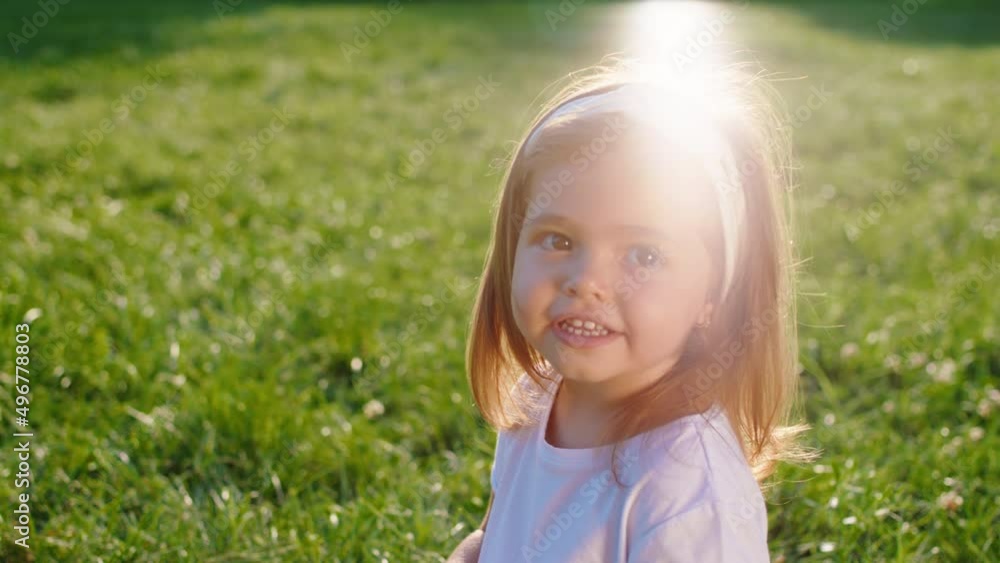 Smiling large cute little girl in front of the camera in a sunny day she looking straight and feeling so happy while sitting in the grass Smiling large cute little girl in front of the camera in a sunny day she looking straight and feeling so happy while sitting in the grass