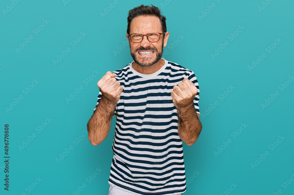 Middle age man wearing casual clothes and glasses very happy and excited doing winner gesture with arms raised, smiling and screaming for success. celebration concept. Middle age man wearing casual clothes and glasses very happy and excited doing winner gesture with arms raised, smiling and screaming for success. celebration concept.