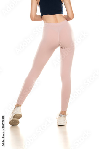 Rear view of a female legs in sport pink tights and sneakers on white background