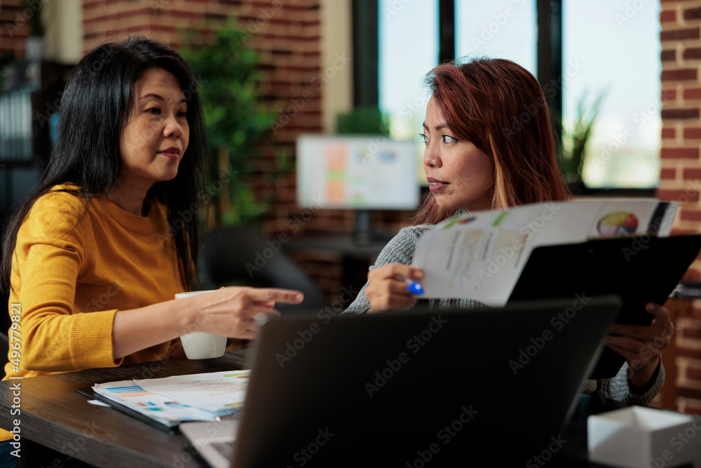 Manager collaborating with businesswoman during business meeting discussing company strategy in startup office. Businesswomen analyzing management graphs working at partnership project Manager collaborating with businesswoman during business meeting discussing company strategy in startup office. Businesswomen analyzing management graphs working at partnership project