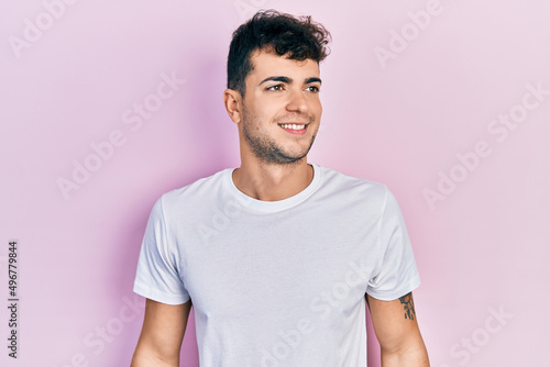 Young hispanic man wearing casual white t shirt looking to side, relax profile pose with natural face and confident smile.