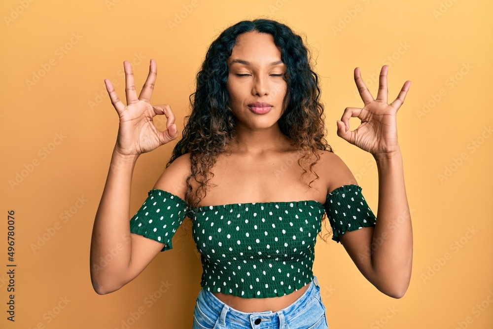Young latin woman wearing casual clothes relax and smiling with eyes closed doing meditation gesture with fingers. yoga concept. Young latin woman wearing casual clothes relax and smiling with eyes closed doing meditation gesture with fingers. yoga concept.