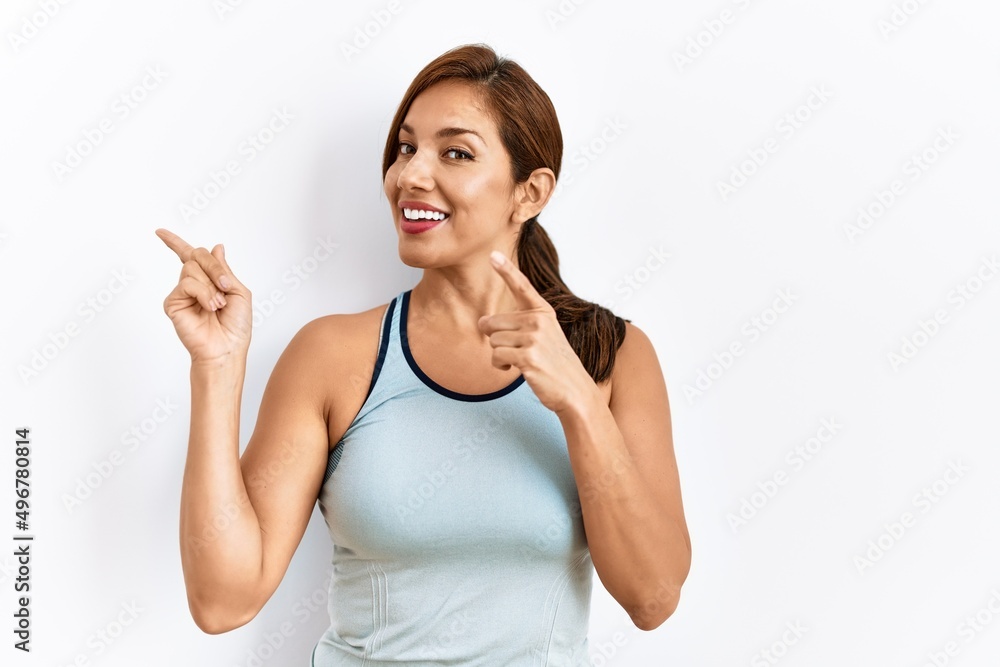 Fototapeta premium Young latin woman wearing sporty clothes over isolated background smiling and looking at the camera pointing with two hands and fingers to the side.