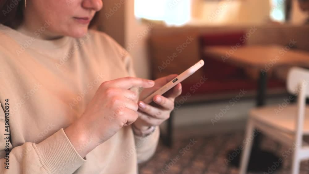 Closeup of a young woman holding and using mobile phone, sitting in cafe texting on the phone Closeup of a young woman holding and using mobile phone, sitting in cafe texting on the phone