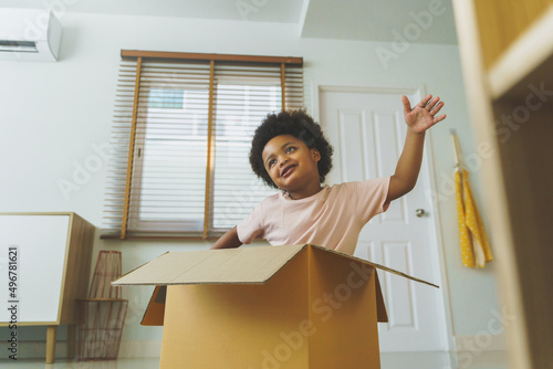 Happy African American Boy curly hair playing with cardboard box while moving house indoors.