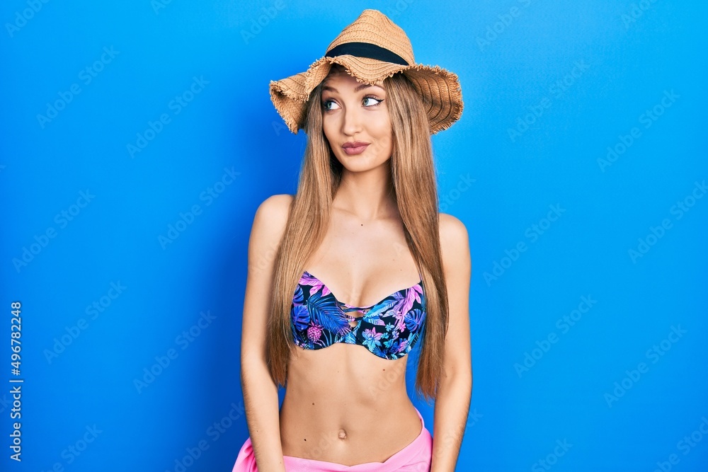 Young blonde girl wearing bikini and summer hat smiling looking to the side and staring away thinking. Young blonde girl wearing bikini and summer hat smiling looking to the side and staring away thinking.