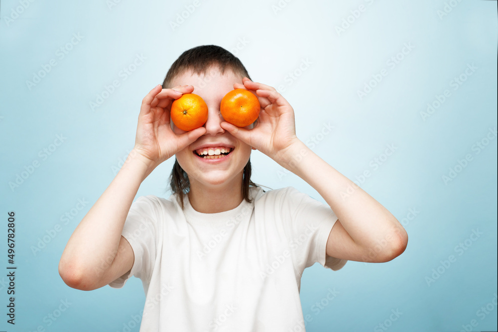 happy smiling boy with two mandarins covering his eyes on blue background. happy smiling boy with two mandarins covering his eyes on blue background.