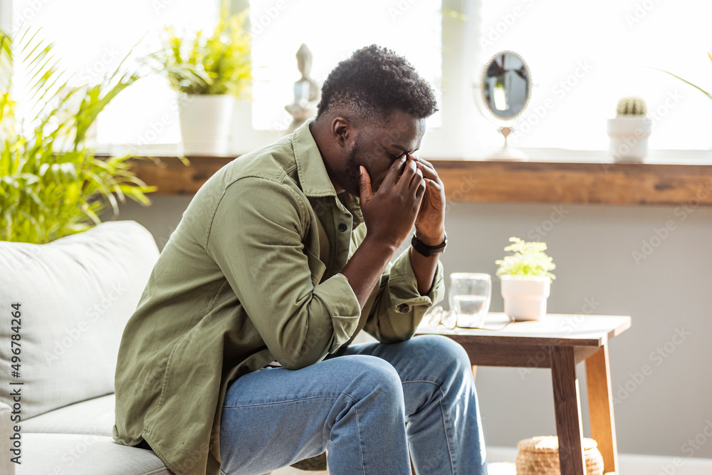 Stressed young african american man feel pain having terrible strong headache concept, tired upset black guy massaging temples suffering from migraine isolated on white grey studio blank background