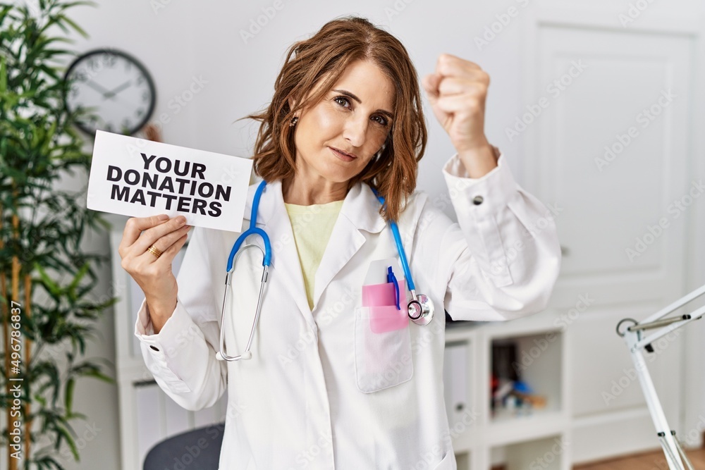 Middle age doctor woman holding your donation matters at the clinic annoyed and frustrated shouting with anger, yelling crazy with anger and hand raised Middle age doctor woman holding your donation matters at the clinic annoyed and frustrated shouting with anger, yelling crazy with anger and hand raised