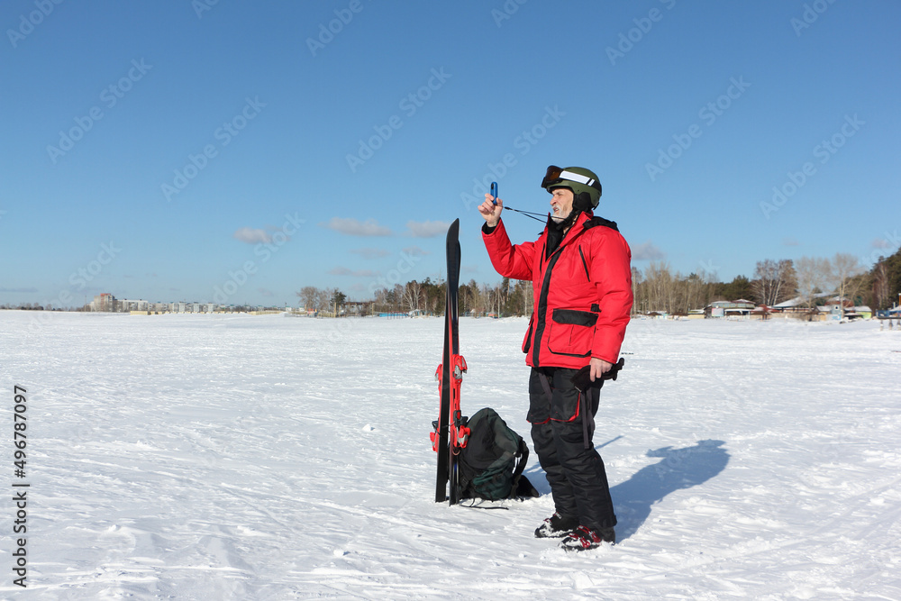 Man in a red jacket with mountain skis measures wind speed with an anemometer in winter