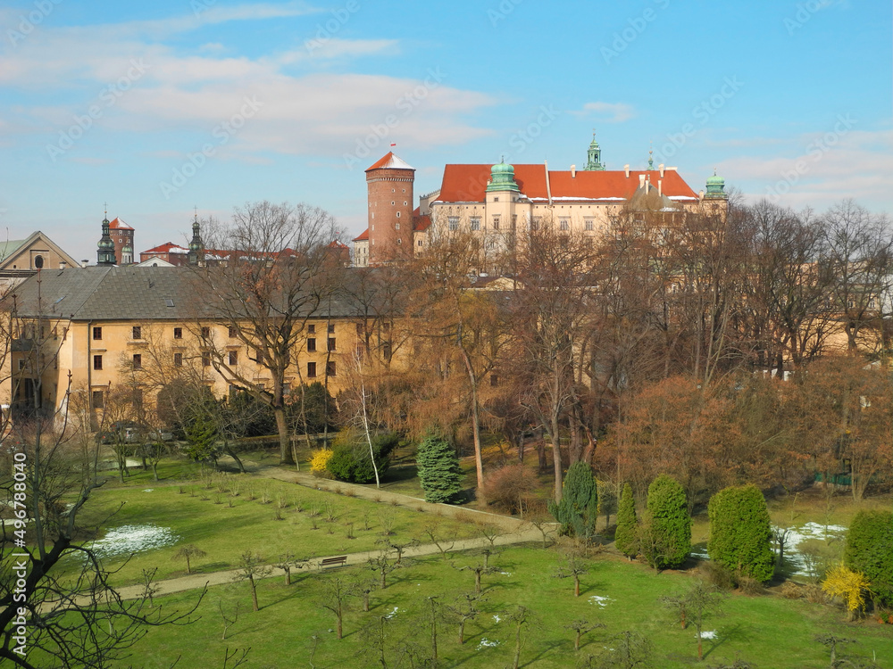 Spring Krakow. Morning view of public park and Wawel Castle from window. Unmelted snow covers green grass and tower roof.