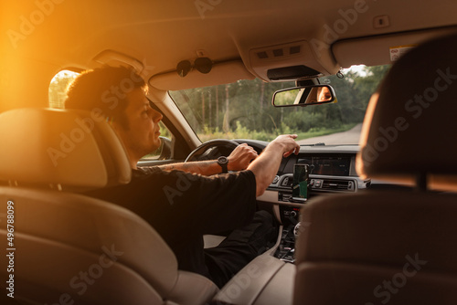 Male driver drives a car in the cabin at sunset