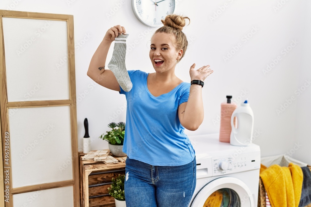 Young caucasian woman holding dirty sock at laundry room waiving saying hello happy and smiling, friendly welcome gesture Young caucasian woman holding dirty sock at laundry room waiving saying hello happy and smiling, friendly welcome gesture