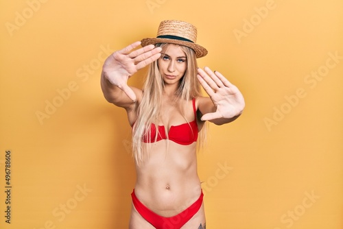 Young caucasian woman wearing bikini and summer hat doing frame using hands palms and fingers, camera perspective