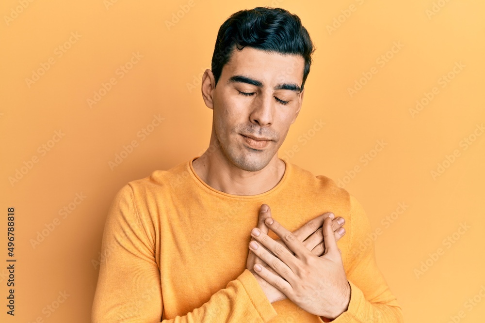 Handsome hispanic man wearing casual clothes smiling with hands on chest, eyes closed with grateful gesture on face. health concept. Handsome hispanic man wearing casual clothes smiling with hands on chest, eyes closed with grateful gesture on face. health concept.