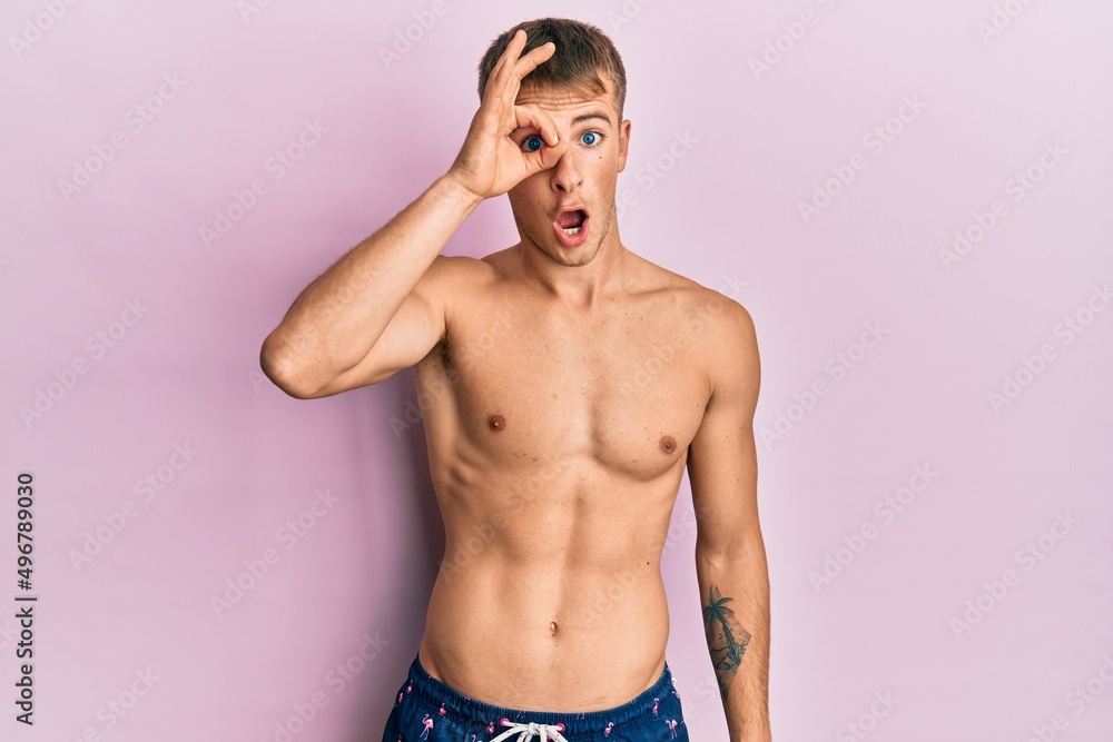 Fototapeta premium Young caucasian man wearing swimwear doing ok gesture shocked with surprised face, eye looking through fingers. unbelieving expression.