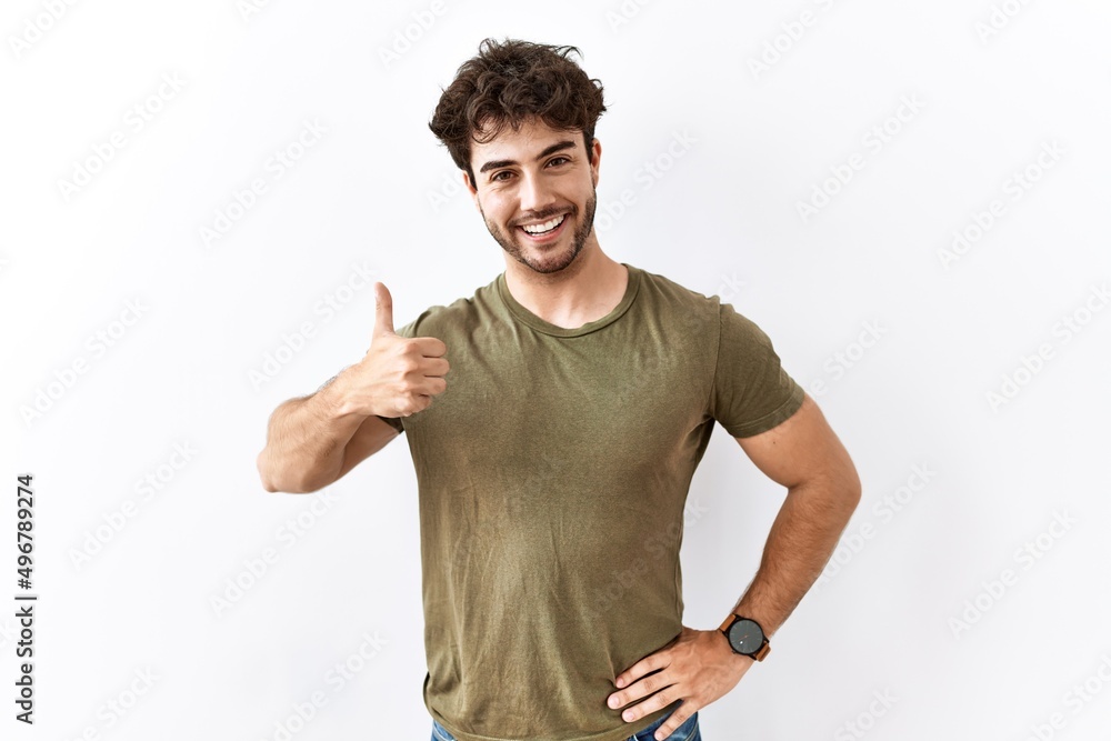 Naklejka premium Hispanic man standing over isolated white background doing happy thumbs up gesture with hand. approving expression looking at the camera showing success.