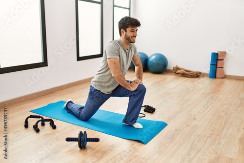 Young hispanic sporty man smiling happy training yoga at sport center.