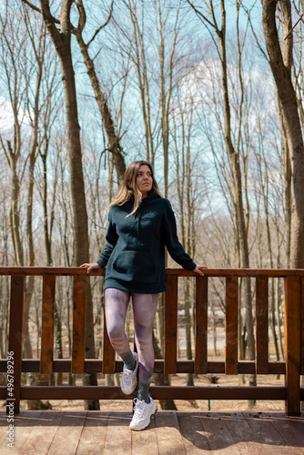 Young woman standing on wooden bridge. She is watching forest view. Travel, sport and hiking concept. Vertical photo.