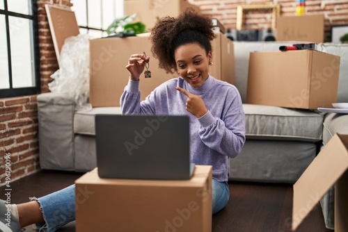 Young african american woman showing keys of new home on video call smiling happy pointing with hand and finger