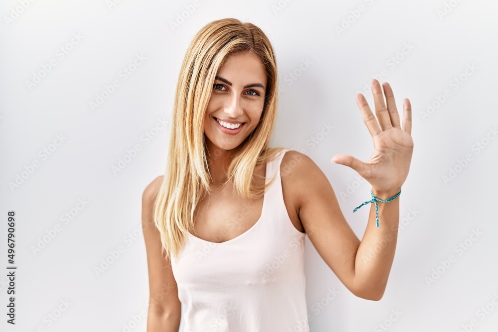 Blonde beautiful young woman standing over white isolated background showing and pointing up with fingers number five while smiling confident and happy. Blonde beautiful young woman standing over white isolated background showing and pointing up with fingers number five while smiling confident and happy.