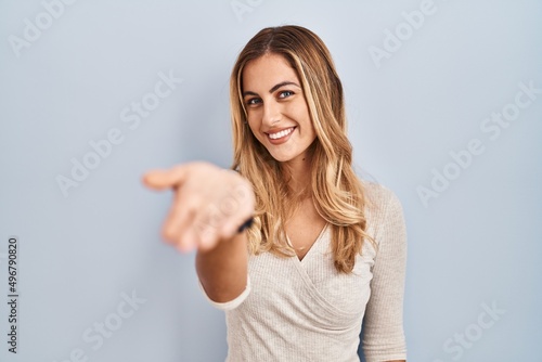 Young blonde woman standing over isolated background smiling cheerful offering palm hand giving assistance and acceptance.