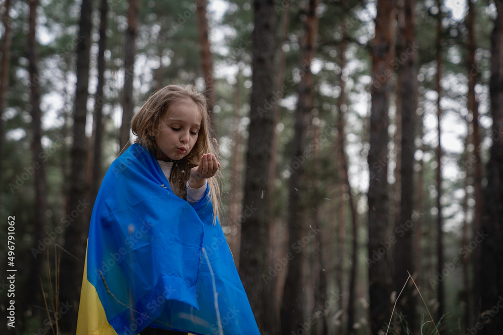 A little girl plays in the forest and hides herself with the flag of Ukraine. Save the children of Ukraine. A little girl plays in the forest and hides herself with the flag of Ukraine. Save the children of Ukraine.