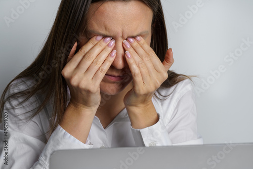 Tired woman suffering from eyes pain after working on the computer. Woman touching painful eyes photo