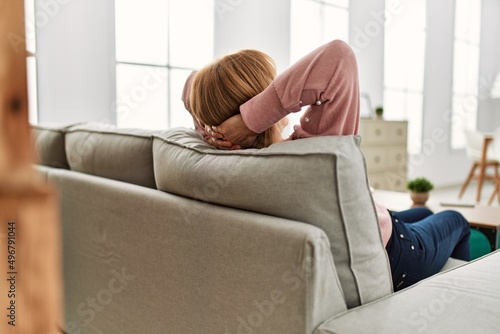 Middle age blonde woman relaxed sitting on the sofa with hands on head at home.