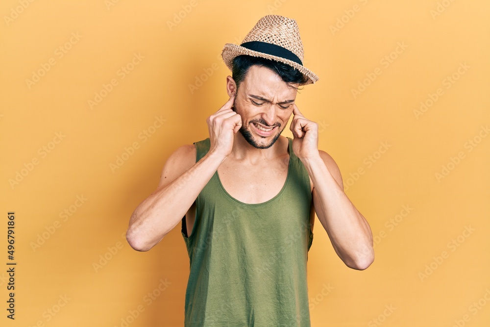Young hispanic man wearing summer hat covering ears with fingers with annoyed expression for the noise of loud music. deaf concept. Young hispanic man wearing summer hat covering ears with fingers with annoyed expression for the noise of loud music. deaf concept.