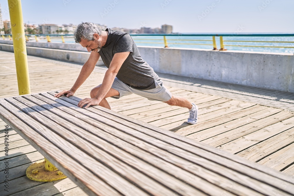 Middle age hispanic man wearing sportswear stretching at seaside