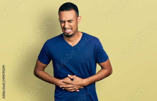 Young african american man wearing casual t shirt with hand on stomach because nausea, painful disease feeling unwell. ache concept.