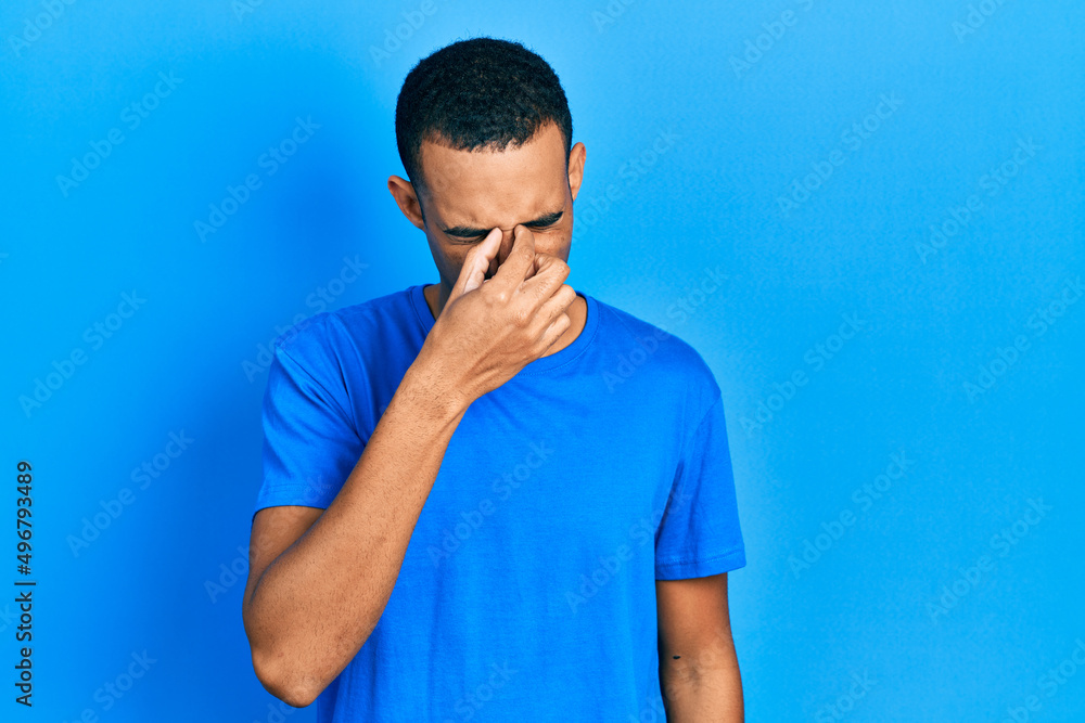 Young african american man wearing casual blue t shirt tired rubbing nose and eyes feeling fatigue and headache. stress and frustration concept. Young african american man wearing casual blue t shirt tired rubbing nose and eyes feeling fatigue and headache. stress and frustration concept.