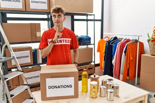 Young caucasian man volunteer holding donations box thinking concentrated about doubt with finger on chin and looking up wondering