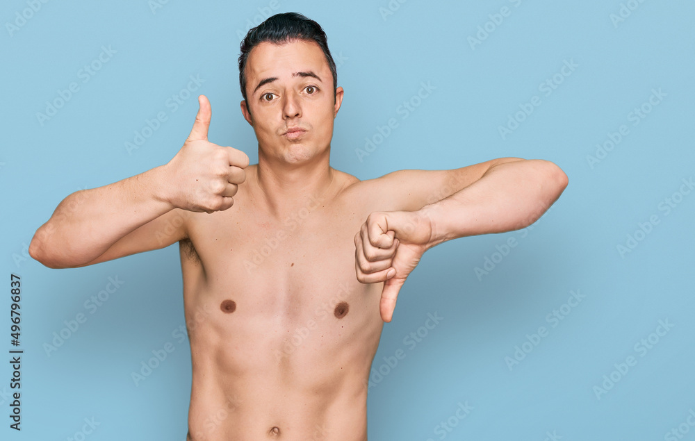 Handsome young man wearing swimwear shirtless doing thumbs up and down, disagreement and agreement expression. crazy conflict Handsome young man wearing swimwear shirtless doing thumbs up and down, disagreement and agreement expression. crazy conflict