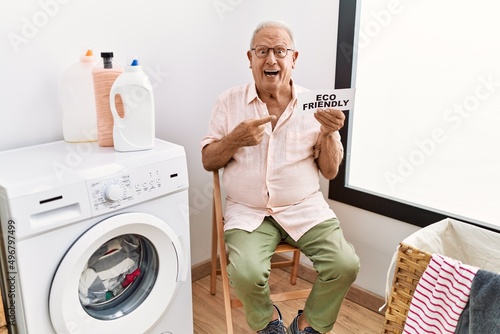 Senior man doing laundry holding eco friendly paper smiling happy pointing with hand and finger