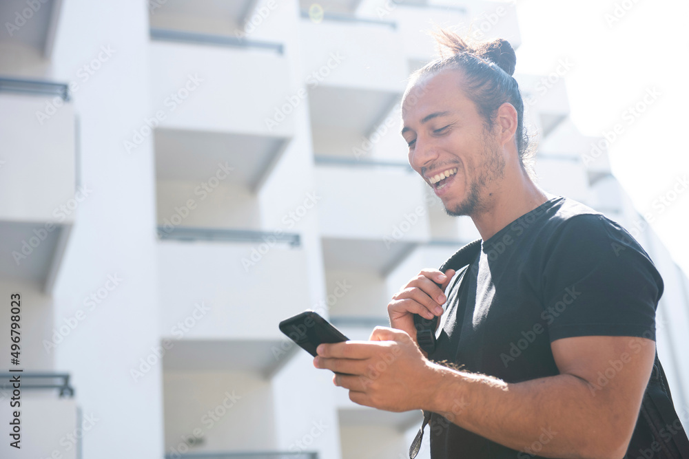 Cheerful man carrying backpack and text messaging using mobile phone outdoors in city Cheerful man carrying backpack and text messaging using mobile phone outdoors in city