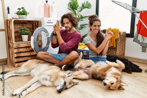 Photography Young hispanic couple doing laundry with dogs holding symbolic gun with hand ges