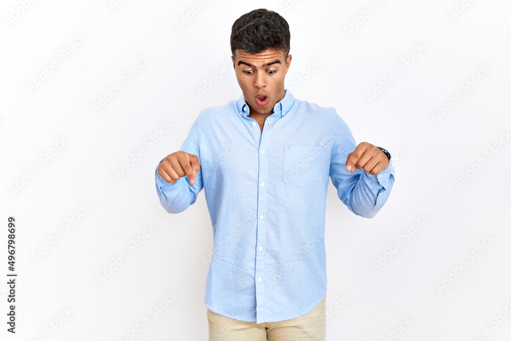 Young hispanic man wearing business shirt standing over isolated background pointing down with fingers showing advertisement, surprised face and open mouth Young hispanic man wearing business shirt standing over isolated background pointing down with fingers showing advertisement, surprised face and open mouth